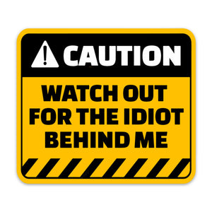 A yellow and black caution sticker with the text 'CAUTION WATCH OUT FOR THE IDIOT BEHIND ME' on it.