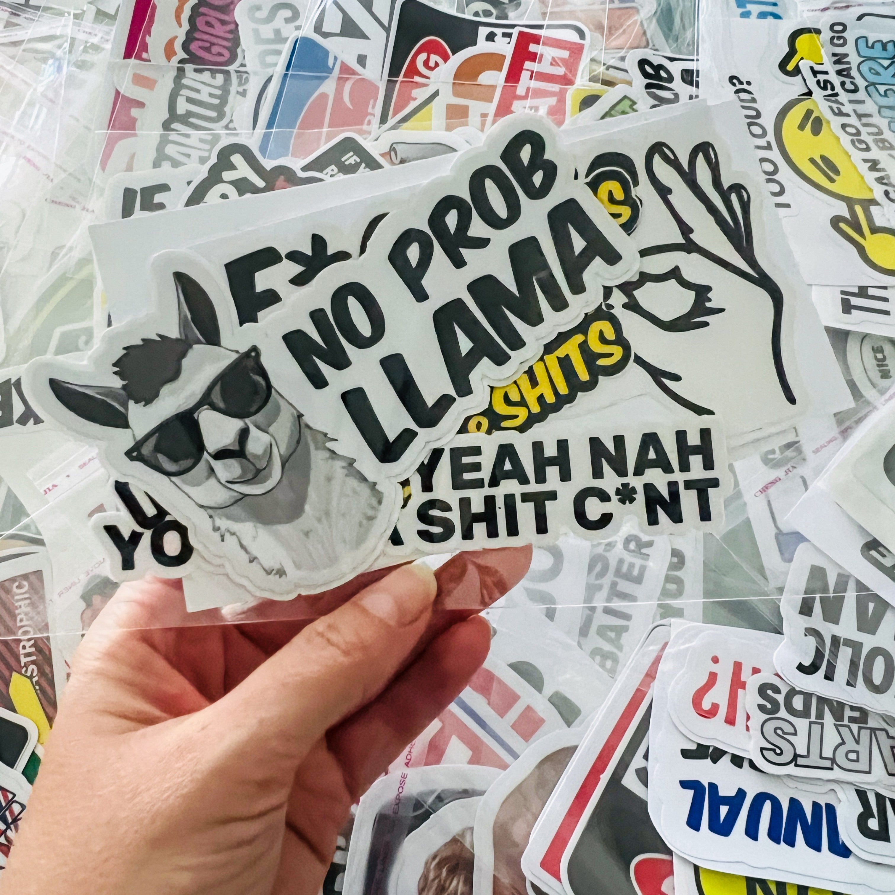 Hand holding a sticker with a llama graphic and text, surrounded by other stickers.