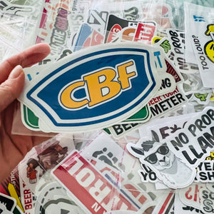 Hand holding a 'CBF' sticker over a collection of various stickers.