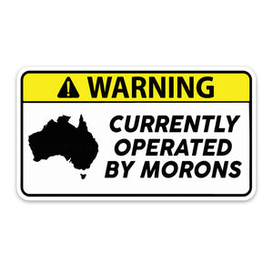A sticker with a black and yellow warning sign that says 'WARNING CURRENTLY OPERATED BY MORONS' with a silhouette of Australia on it.