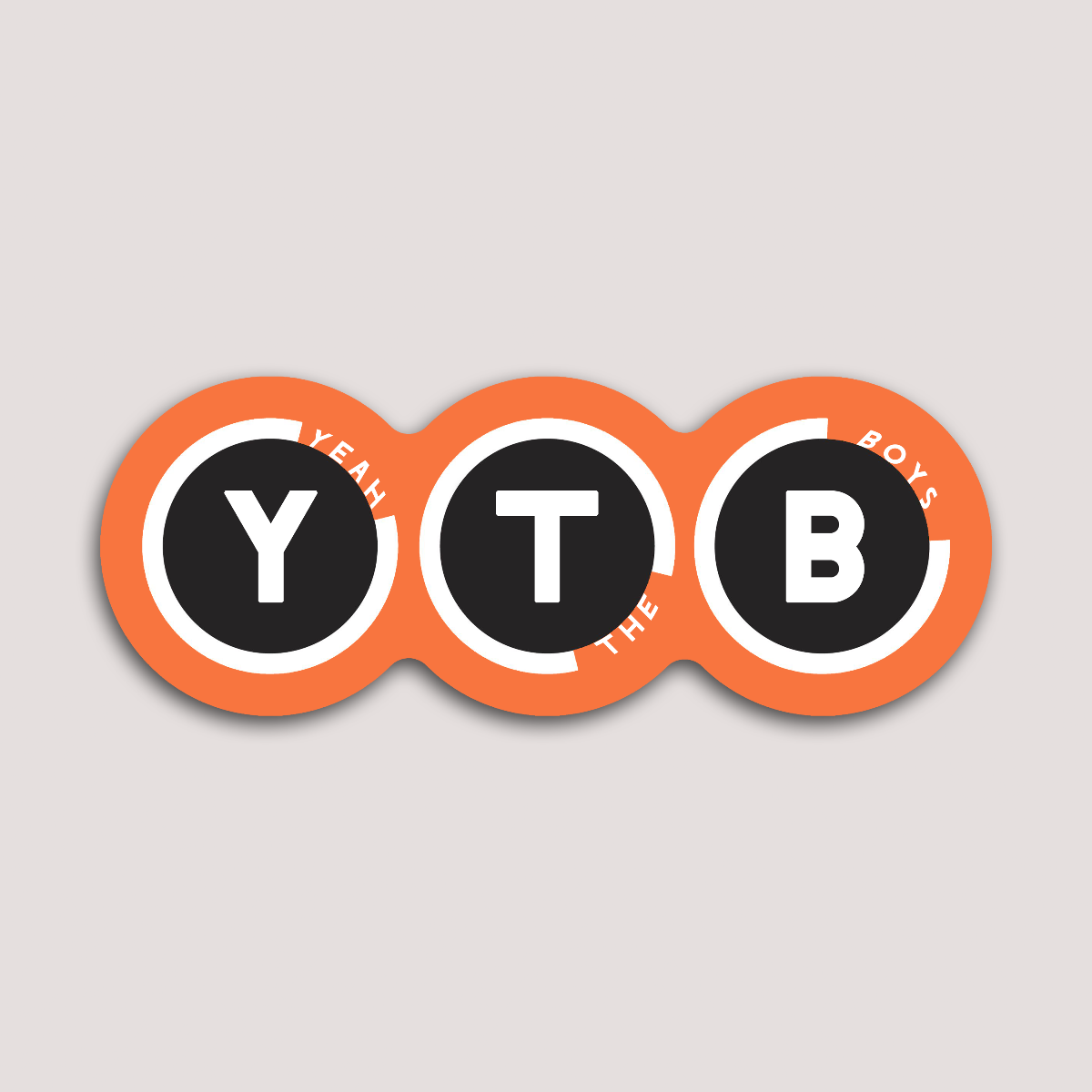 A round sticker with the letters 'YTB' in white font placed against an orange background, with the phrase 'Yeah The Boys'.